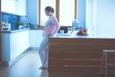 Cep telefonu ayakta modern mutfak kullanan kadın.