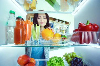 Sağlıklı yiyecek, sebze ve meyvelerle dolu açık buzdolabının yanında duran kadın portresi. Kadın portresi