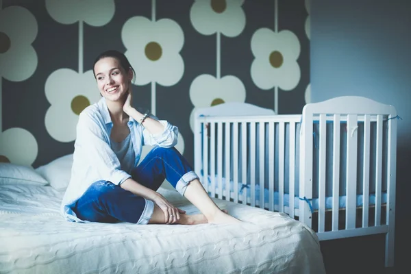 子供のベッドの近くにベッドに座っている若い女性。若いママ — ストック写真