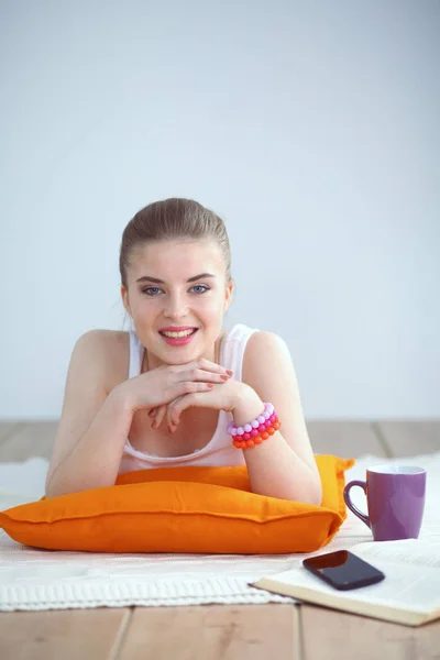 Smiling young woman lying on a white floor with pillow. — Stock Photo, Image