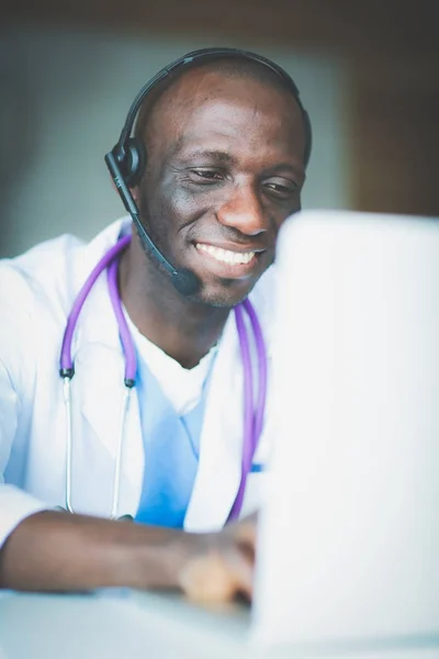 Портрет молодого чоловіка-лікаря, який носить гарнітуру під час використання комп'ютера за столом у клініці. Лікар . — стокове фото
