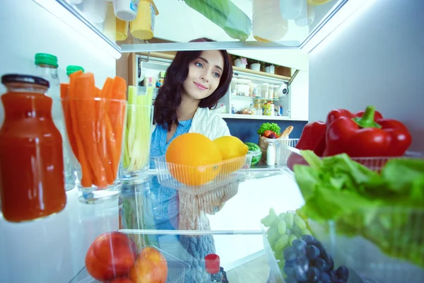 Retrato de una mujer parada cerca de una nevera abierta llena de alimentos saludables, verduras y frutas. Retrato de mujer — Foto de Stock