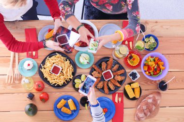 Ahşap masada otururken birlikte yemek yiyen bir grup insanın üst düzey görüntüsü. Masada yemek var. İnsanlar fast food yiyor. Yemek fotoğrafı.