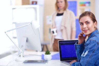 İki genç kadın masada enstrümanlar, planlar ve dizüstü bilgisayarlarla oturuyor..