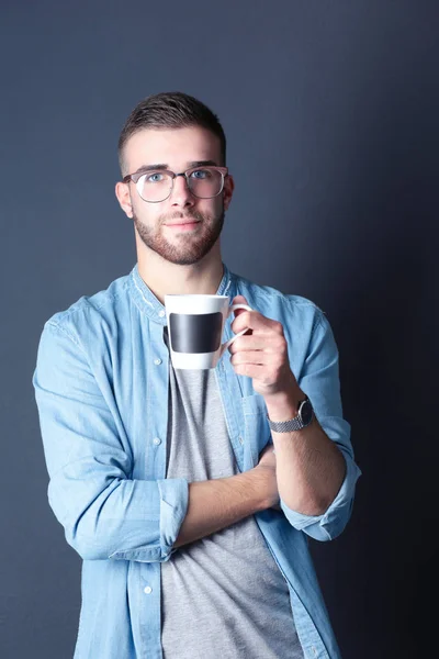 Portret van een knappe jongeman permanent en houden van een kopje koffie in zijn handen — Stockfoto