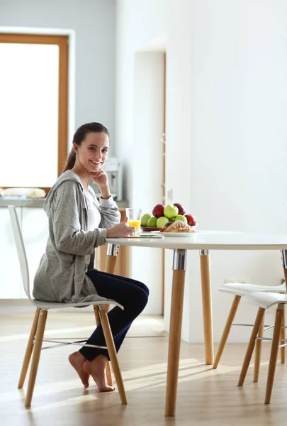 Mujer joven con jugo de naranja y tableta en la cocina. — Foto de Stock