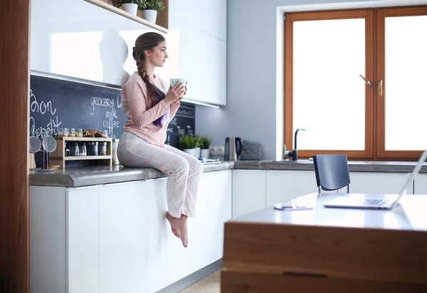 Ung kvinna sitter på bord i köket. — Stockfoto