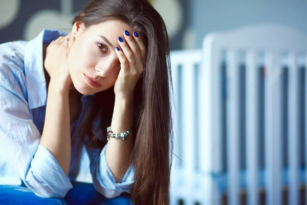 Ung trött kvinna som sitter på sängen nära barnens spjälsäng. Ung mamma. — Stockfoto