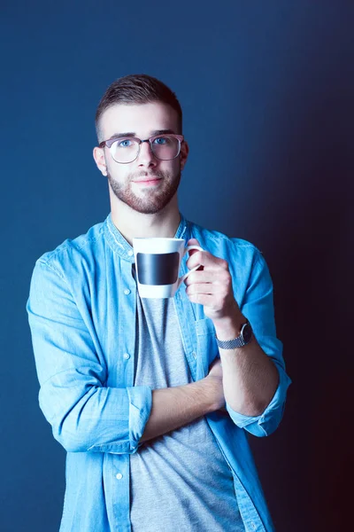 Retrato de un joven guapo de pie y sosteniendo una taza de café en sus manos — Foto de Stock