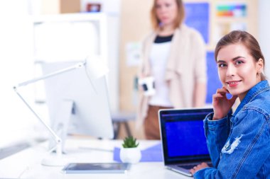 İki genç kadın masada enstrümanlar, planlar ve dizüstü bilgisayarlarla oturuyor..