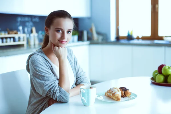 Kvinna som dricker te med söt croissant på köksbordet. — Stockfoto