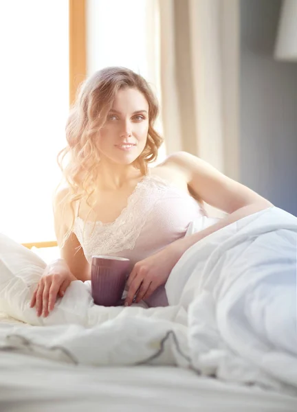 Jonge vrouw kopje koffie of thee drinken terwijl liggend in bed. — Stockfoto