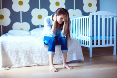 Genç çocuk karyolası yakın yatağın üstüne oturan kadın yorgun. Genç anne.