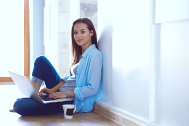 Dizüstü bilgisayar ile yerdeki genç güzel kadın evde oturuyor. Genç güzel kadın.