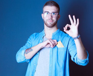 Gri arka planda duran bir kredi kartı tutan genç adam. Genç girişimci..