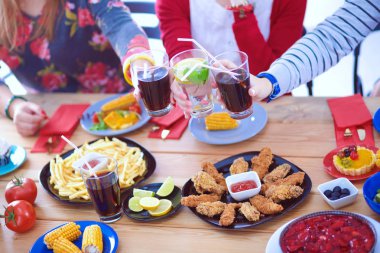 Ahşap masada otururken birlikte yemek yiyen bir grup insanın üst düzey görüntüsü. Masada yemek var. İnsanlar fast food yiyor..