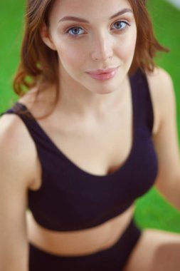 Yeşil çimenlerin üzerinde çapraz ayaklı oturan kadın.