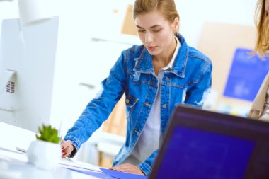 Masanın yanında duran iki genç kadın enstrüman, plan ve dizüstü bilgisayarla.