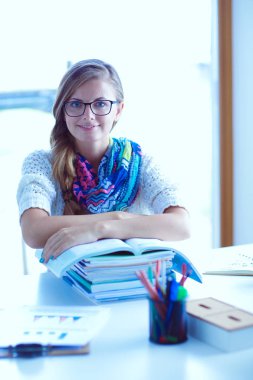 Kitapların arasında bir masada oturan genç bir kadın. Öğrenci