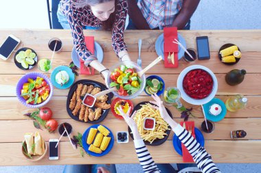 Ahşap masada otururken birlikte yemek yiyen bir grup insanın üst düzey görüntüsü. Masada yemek var. İnsanlar fast food yiyor..