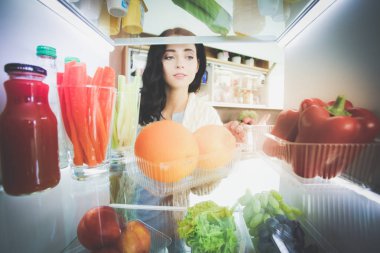 Sağlıklı yiyecek, sebze ve meyvelerle dolu açık buzdolabının yanında duran kadın portresi. Kadın portresi