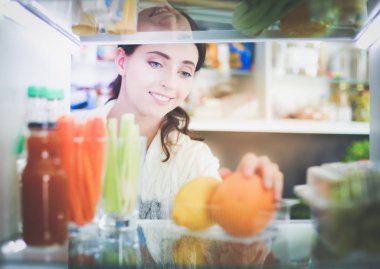 Sağlıklı yiyecek, sebze ve meyvelerle dolu açık buzdolabının yanında duran kadın portresi. Kadın portresi