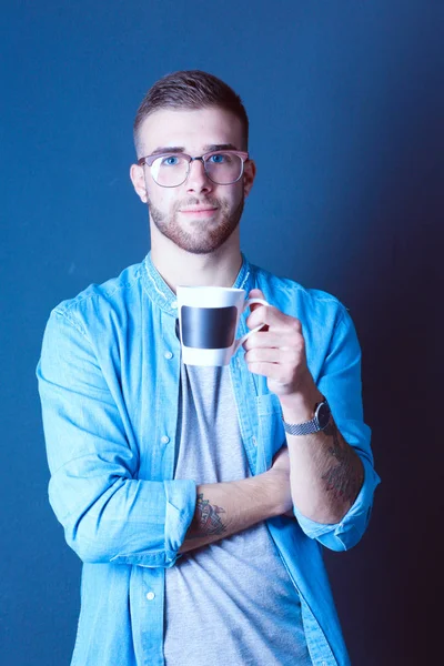 Retrato de um jovem bonito de pé e segurando uma xícara de café em suas mãos — Fotografia de Stock