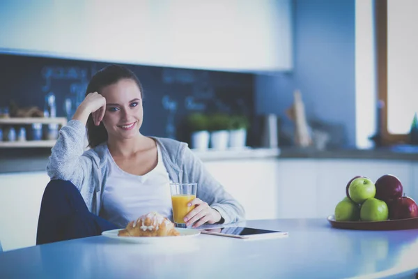 Mujer joven con jugo de naranja y tableta en la cocina. —  Fotos de Stock