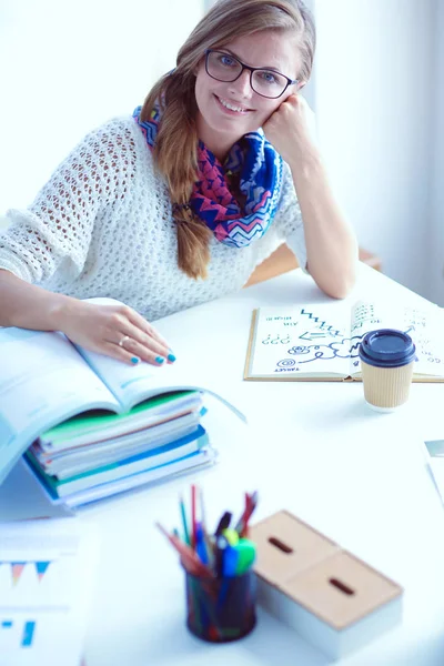 Giovane donna seduta ad una scrivania tra i libri. Studente — Foto Stock