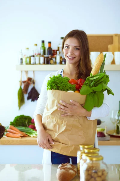 Jovem segurando bolsa de compras de supermercado com legumes. De pé na cozinha. Jovem mulher — Fotografia de Stock