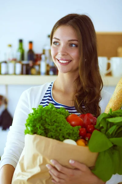 Mujer joven sosteniendo bolsa de la compra de comestibles con verduras.De pie en la cocina. Mujer joven — Foto de Stock