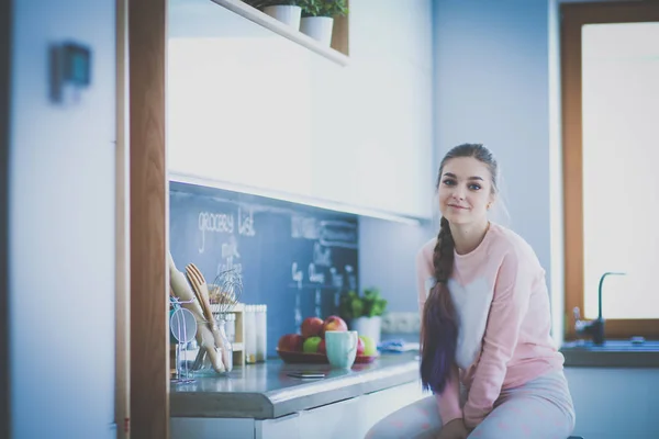 Young woman sitting on table in the kitchen. — Stock Photo, Image