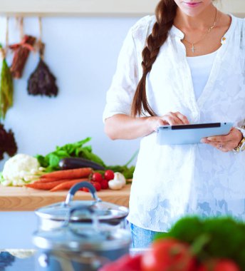 Mutfakta yemek yapmak için tablet bilgisayar kullanan genç bir kadın.