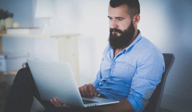 Yakışıklı genç adam dizüstü bilgisayarda oturuyor ve çalışıyor.