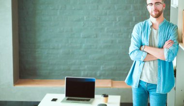 Duvarın yanında dizüstü bilgisayar tutan genç adam.