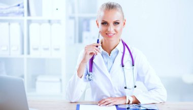 Güzel, genç, gülümseyen bayan doktor masada oturuyor ve yazıyor..