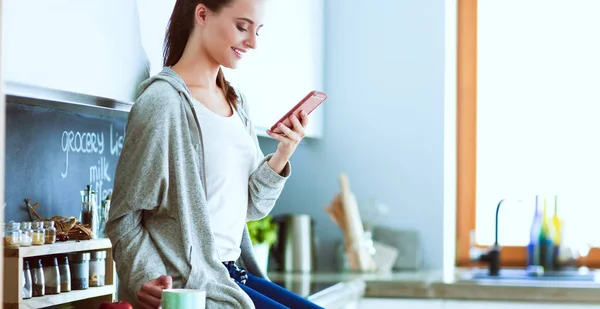 Vrouw met behulp van mobiele telefoon zitten in moderne keuken — Stockfoto