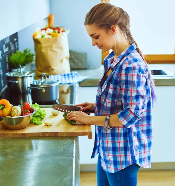 Jonge vrouw snijden van groenten in de keuken in de buurt van bureau — Stockfoto