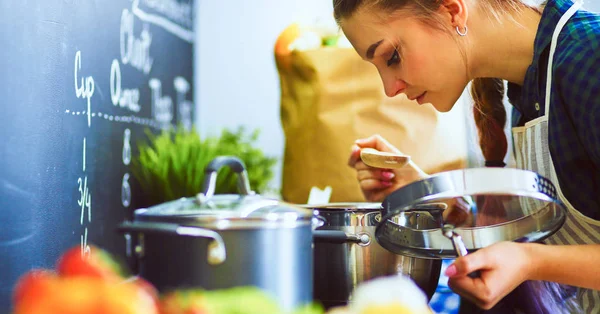 Mujer joven parada junto a la estufa en la cocina — Foto de Stock