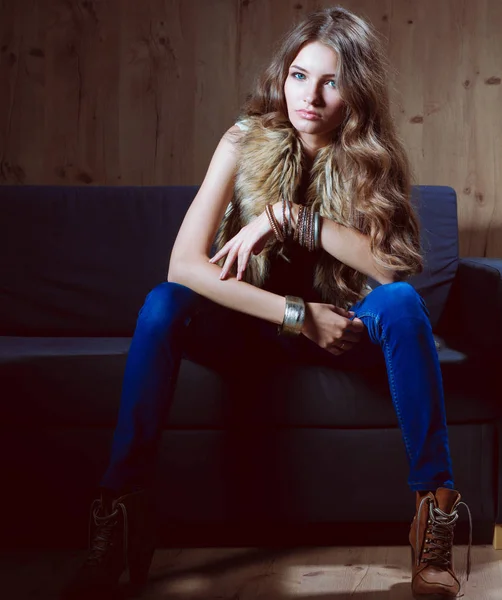 Retrato de mulher elegante sentado no sofá preto vestindo uma calça azul e colete de pele — Fotografia de Stock