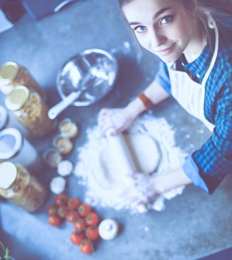Güzel bir kadın mutfakta pasta pişiriyor. Masanın yanında duruyor.