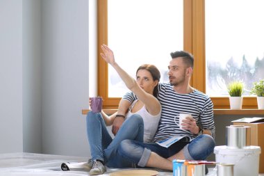 Yeni evin içini boyayan mutlu, gülümseyen genç bir çift portresi. Genç çift