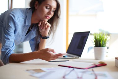 Ofis masasında oturan ve cep telefonuyla konuşan genç ve güzel bir iş kadını. İş kadını