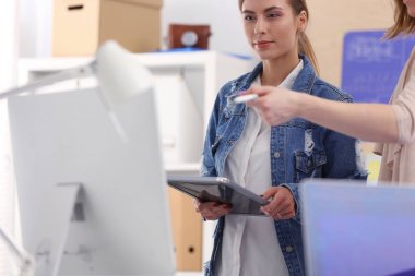 Masanın yanında duran iki genç kadın enstrüman, plan ve dizüstü bilgisayarla.