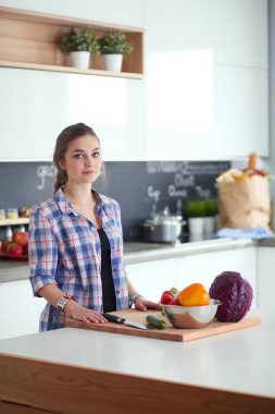 Masanın yanındaki mutfakta sebze doğrayan genç bir kadın..
