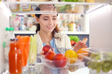 Sağlıklı yiyecek, sebze ve meyvelerle dolu açık buzdolabının yanında duran kadın portresi. Kadın portresi