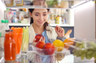 Sağlıklı yiyecek, sebze ve meyvelerle dolu açık buzdolabının yanında duran kadın portresi. Kadın portresi