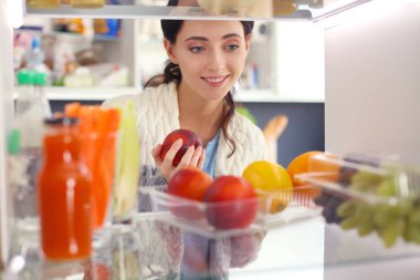 Sağlıklı yiyecek, sebze ve meyvelerle dolu açık buzdolabının yanında duran kadın portresi. Kadın portresi