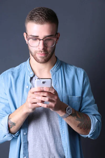 Mosolyogva fiatalember gazdaság telefon, miközben a szöveges üzenetek — Stock Fotó