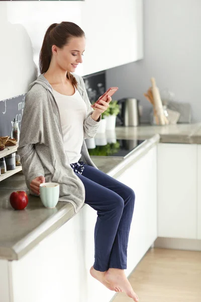 Vrouw met behulp van mobiele telefoon zitten in moderne keuken. — Stockfoto